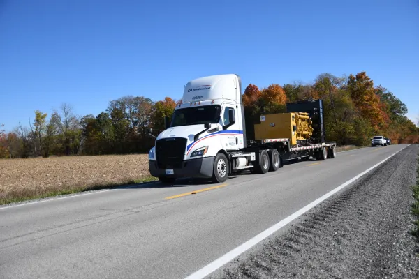 Specialized freight service truck hauling heavy equipment on flatbed trailer