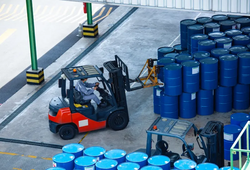 Forklift loading blue chemical barrels in a warehouse for dedicated chemical logistics transportation