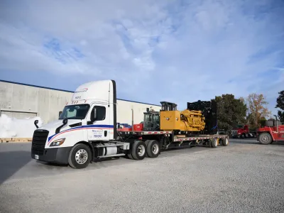 Flatbed semi truck hauling heavy industrial generator equipment for heavy haul shipping and freight services