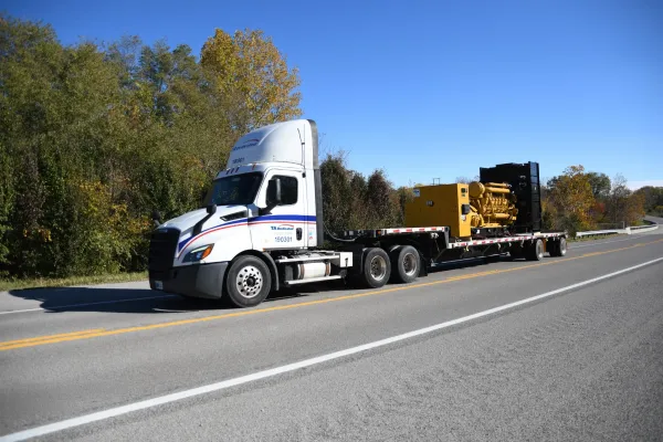 Flatbed truck transporting heavy industrial equipment on highway for secure equipment transport services