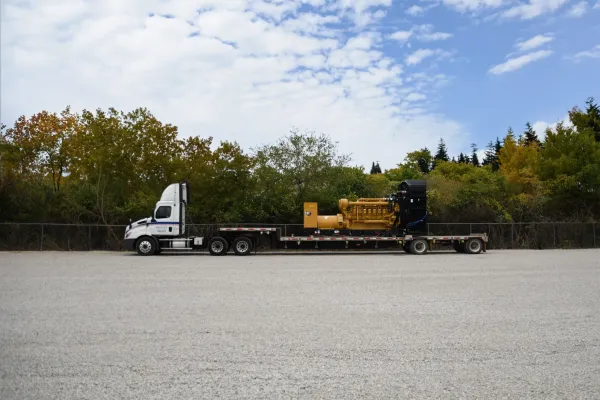 Flatbed truck delivering CAT industrial generator to job site for on-site logistics and equipment delivery services