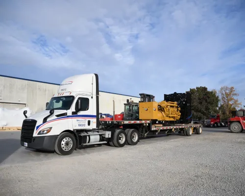 Flatbed semi truck hauling heavy industrial generator equipment for heavy haul shipping and freight services