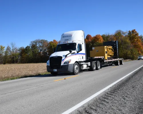 Specialized freight service truck hauling heavy equipment on flatbed trailer